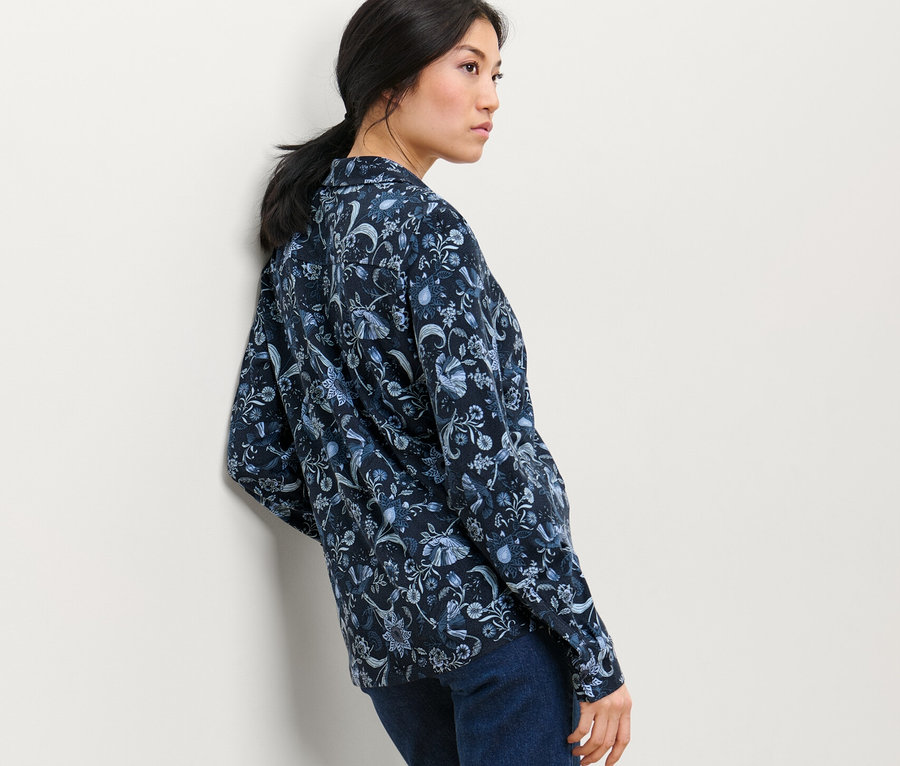 Femme posant dans un chemisier imprimé avec patte de boutonnage et un jean.