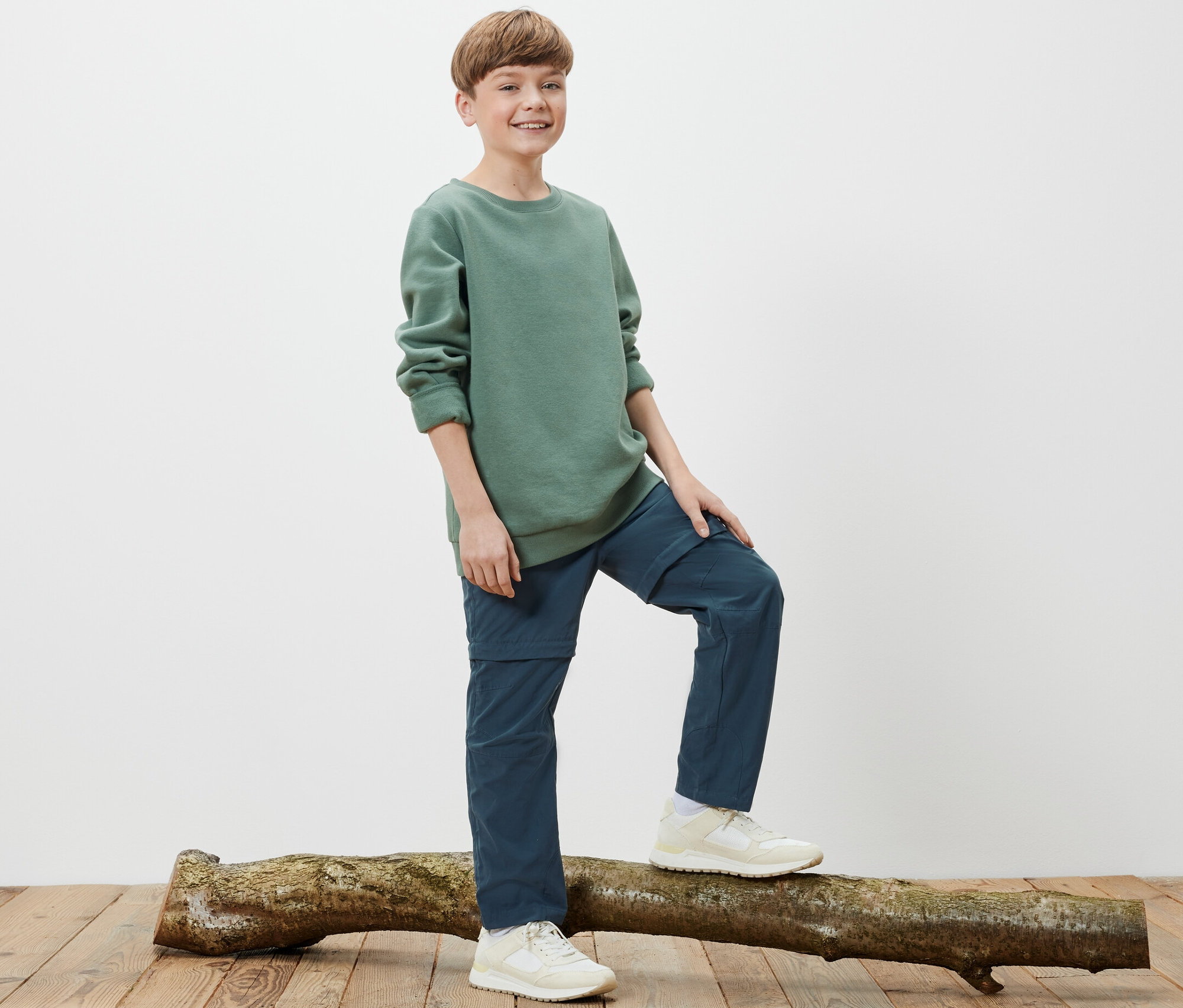 Un garçon se tient sur un tronc d'arbre et porte un pantalon fonctionnel pour enfant.