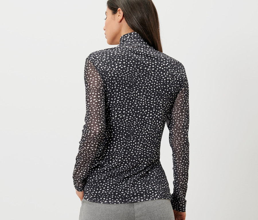 Vue arrière d'une femme aux cheveux foncés portant une chemise à col roulé en mesh avec pois.