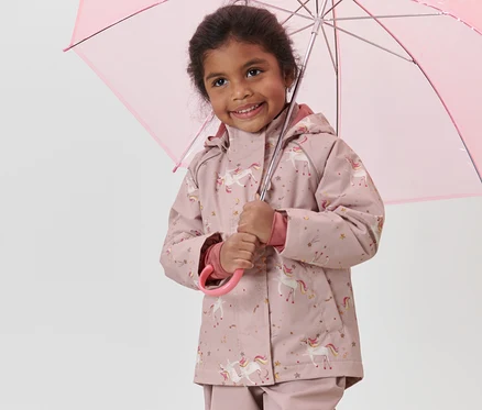 Fillette souriante tenant un parapluie rose et portant une veste de pluie thermique rose pour enfant avec motif de licorne.