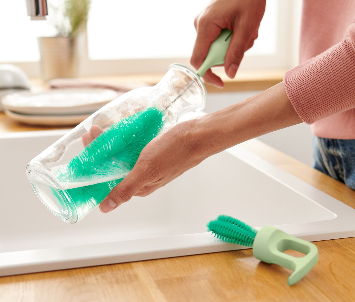 Une femme nettoie une bouteille en verre avec une brosse à vaisselle pour verres et bouteilles 3 en 1.