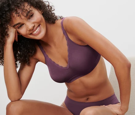 Femme assise sur une chaise portant un soutien-gorge doux Seamless aubergine et une culotte assortie.