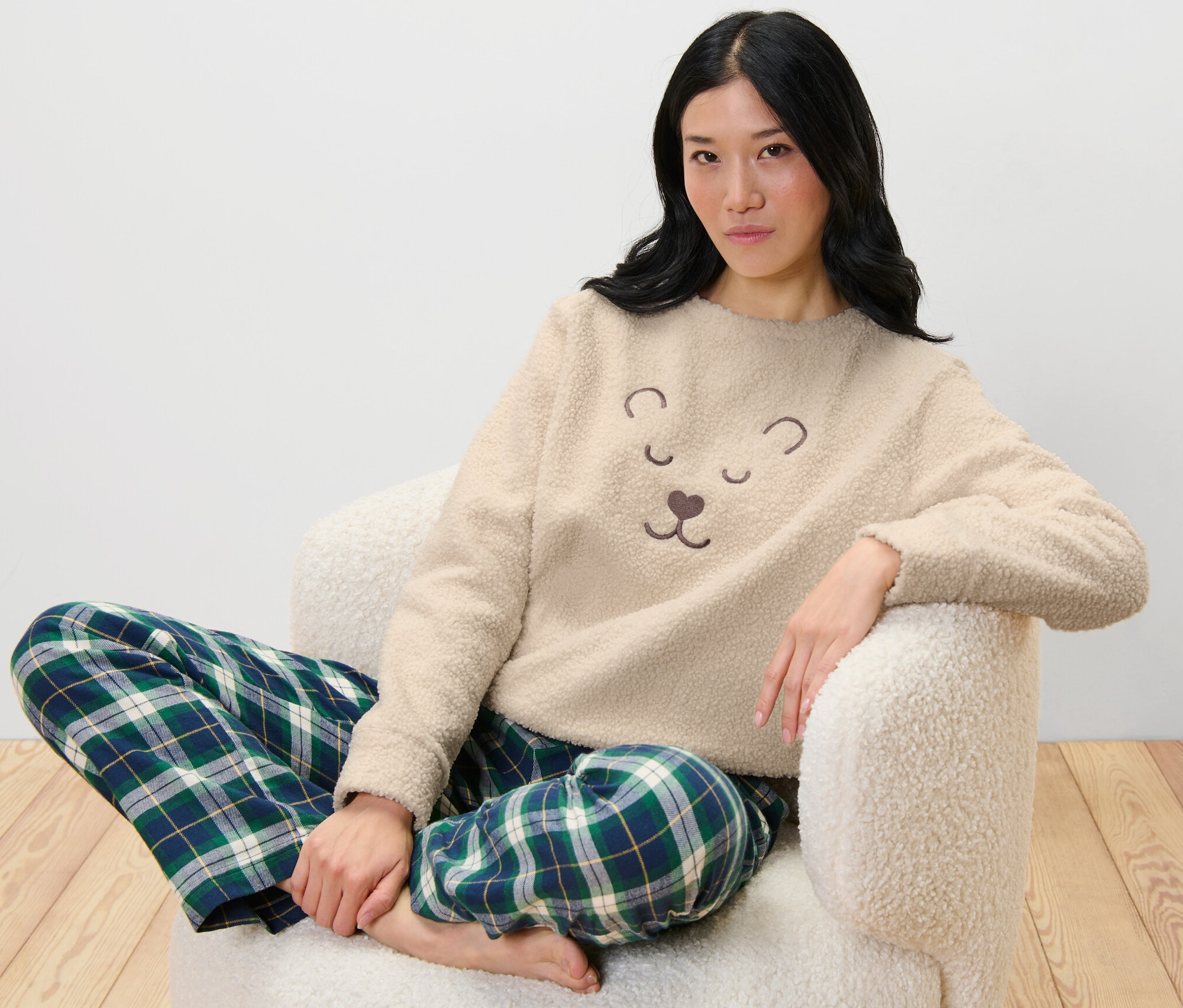 Une femme est assise dans un fauteuil et porte un Sweatshirt moelleux et un pantalon à carreaux.