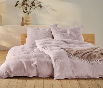 Parure de lit en mousseline rose de taille standard et grande taille sur un lit avec cadre en bois.