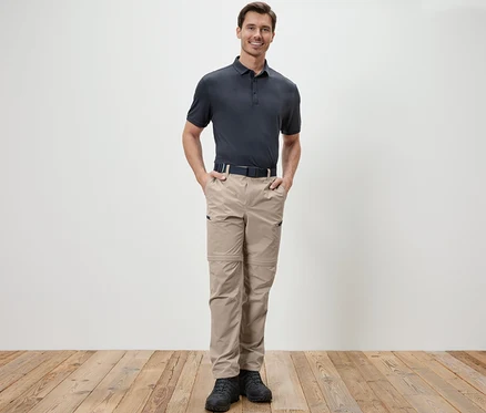 Un homme debout, les mains dans les poches d'un pantalon technique 2 en 1 beige.