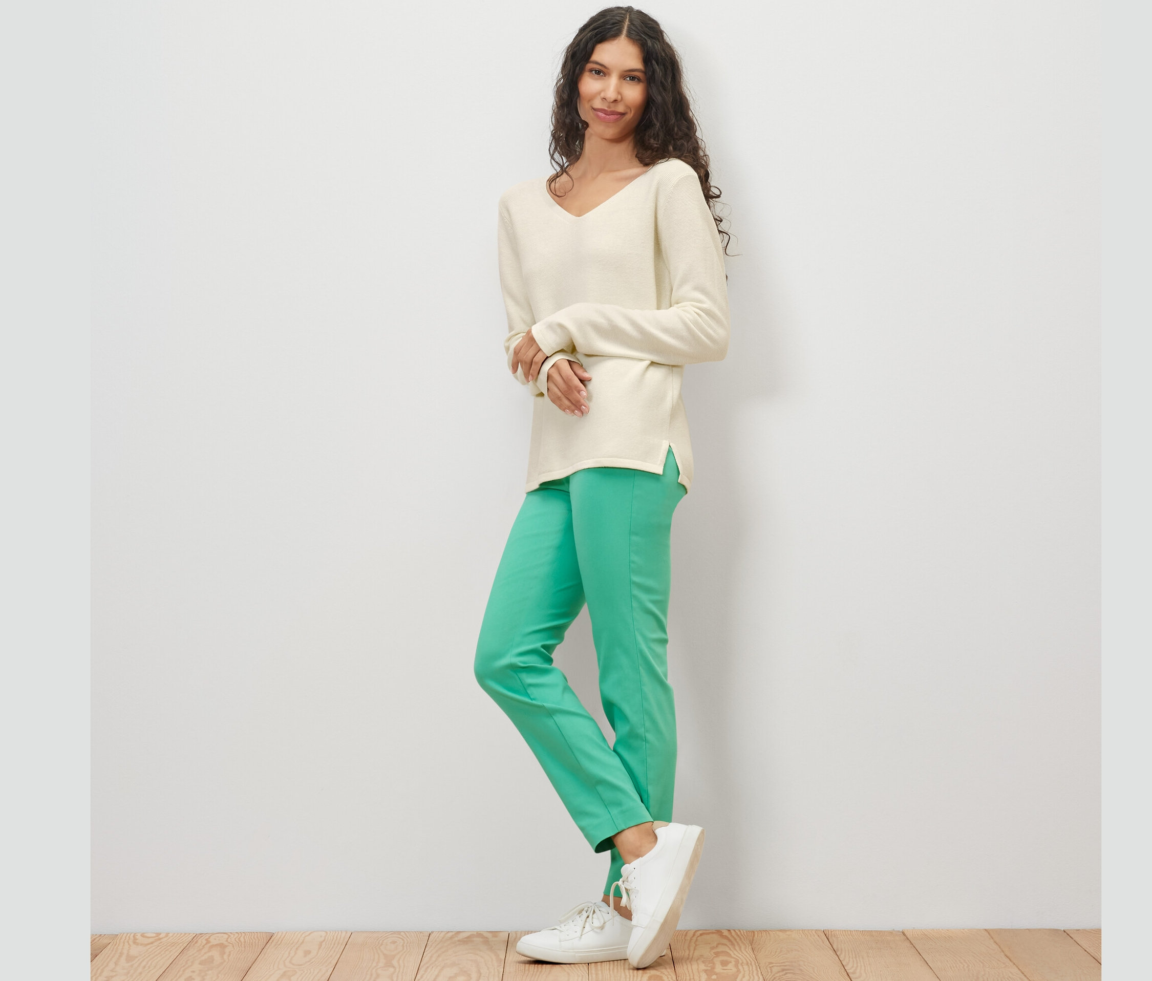 Une femme pose sur un fond clair et porte un pull en maille blanc crème.