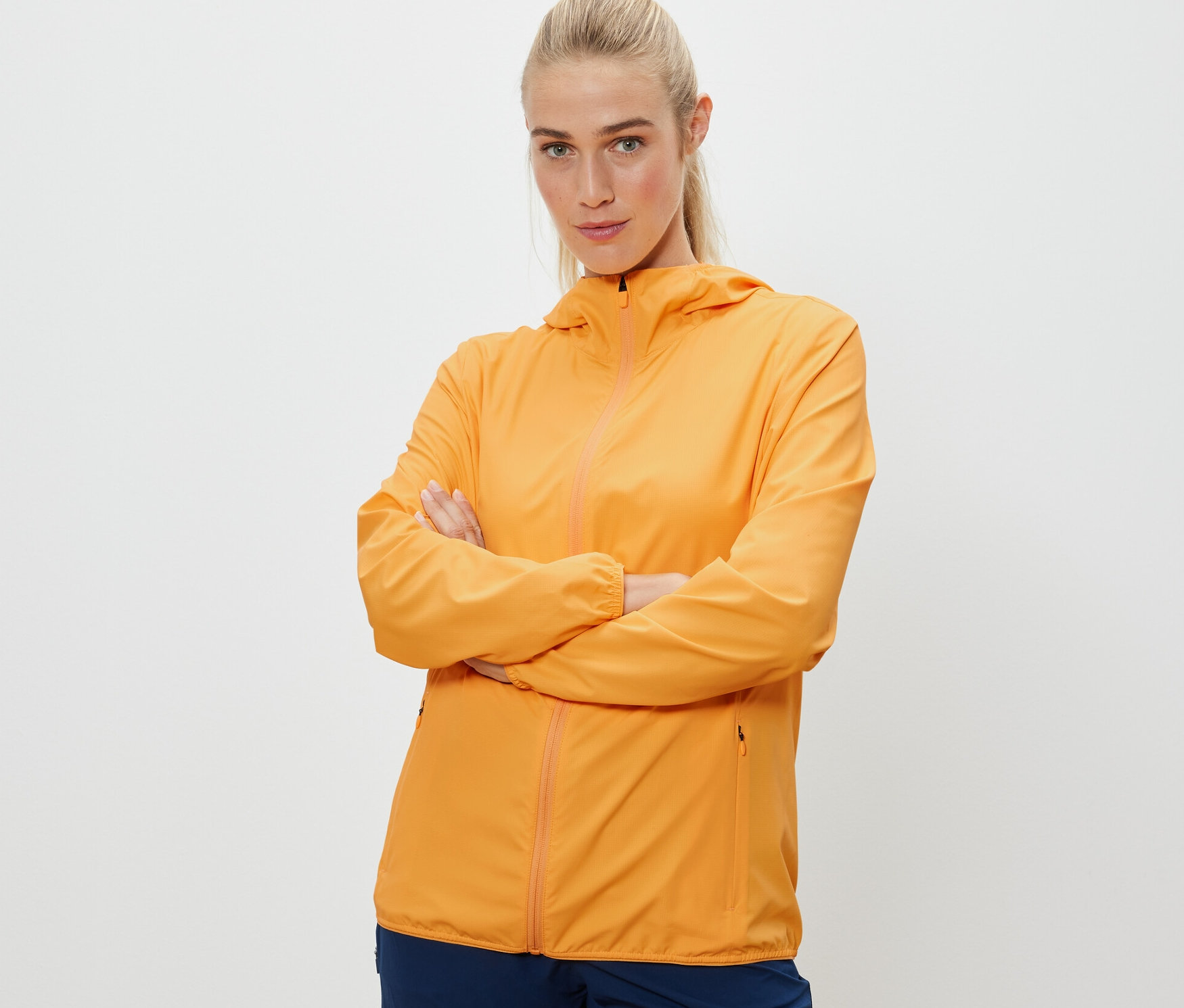 Femme posant les bras croisés portant une veste fonctionnelle pliable orange.