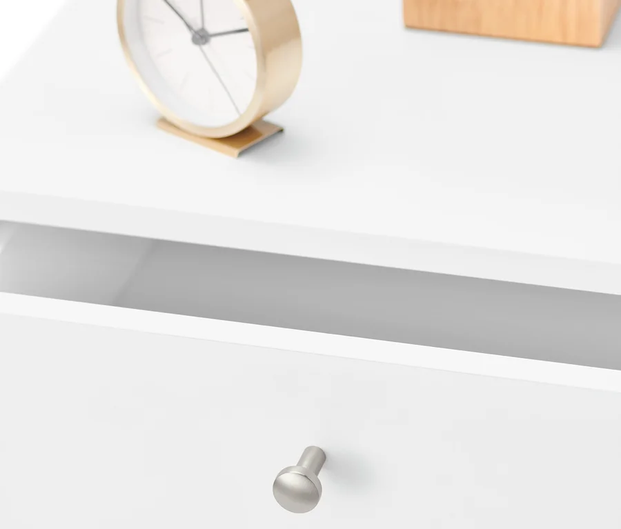 Gros plan d'une table de chevet blanche avec un tiroir ouvert, une horloge dorée et une boîte en bois. Table de chevet.