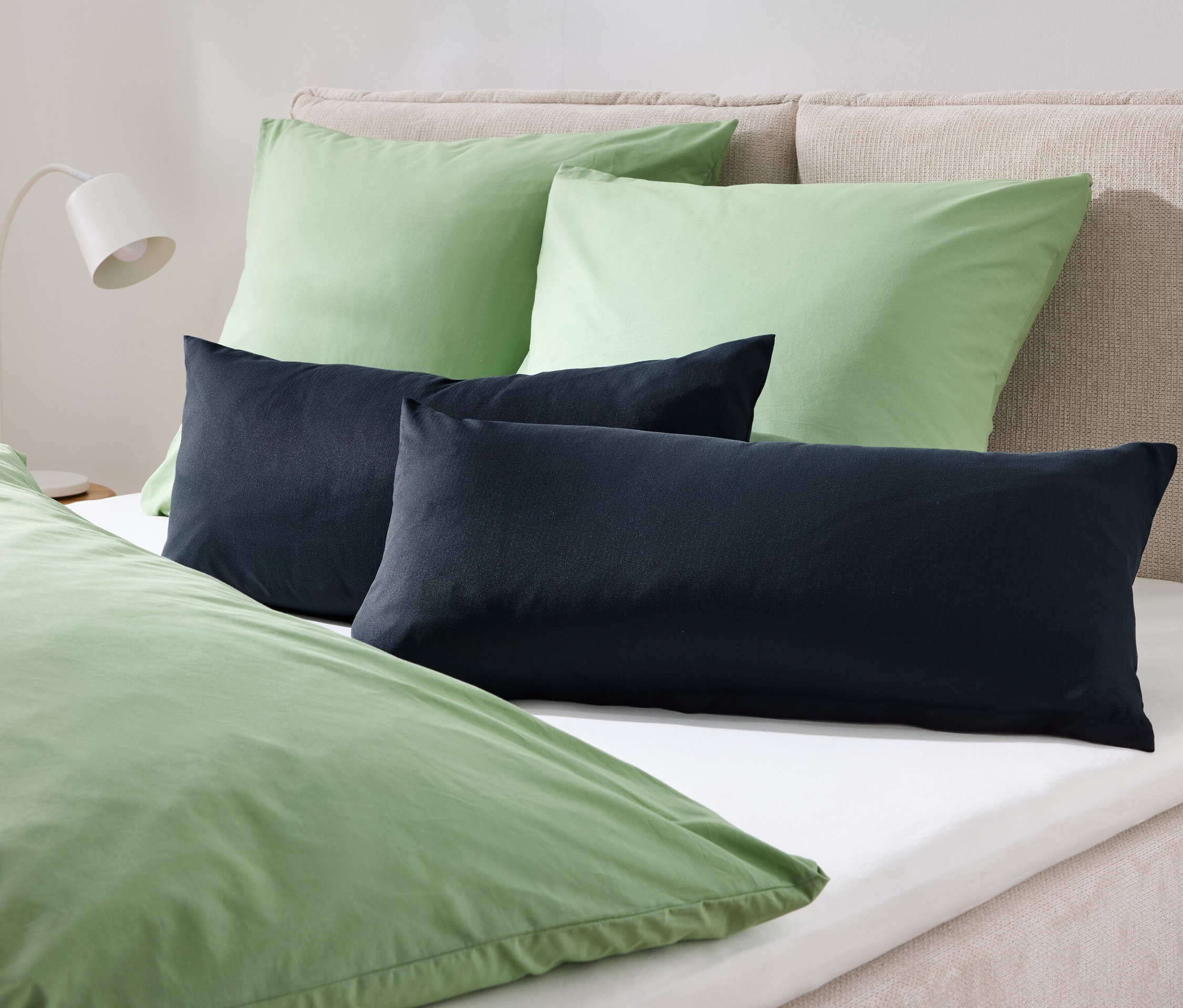 Sur un lit, deux oreillers verts et deux oreillers bleu foncé recouverts d'une literie verte.