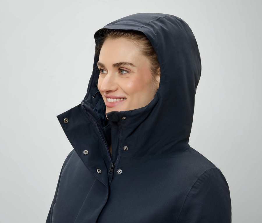 Une femme avec une capuche et une veste bleu marine regarde vers la droite.