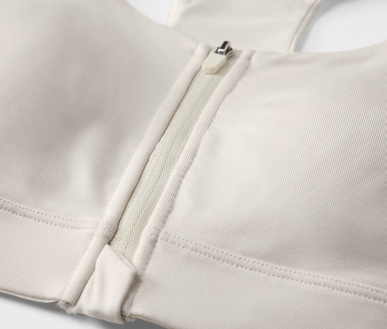 Gros plan d'un soutien-gorge de sport blanc cassé avec fermeture éclair sur le devant.