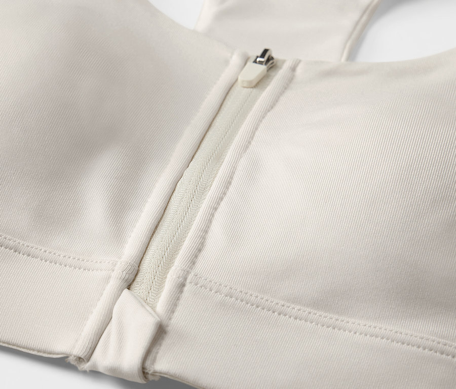 Gros plan d'un soutien-gorge de sport blanc cassé avec fermeture éclair sur le devant.