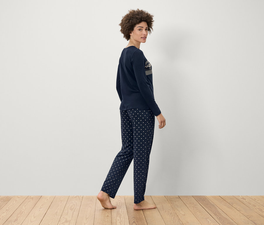 Femme marchant en pyjama bleu marine à pois blancs sur un plancher en bois.
