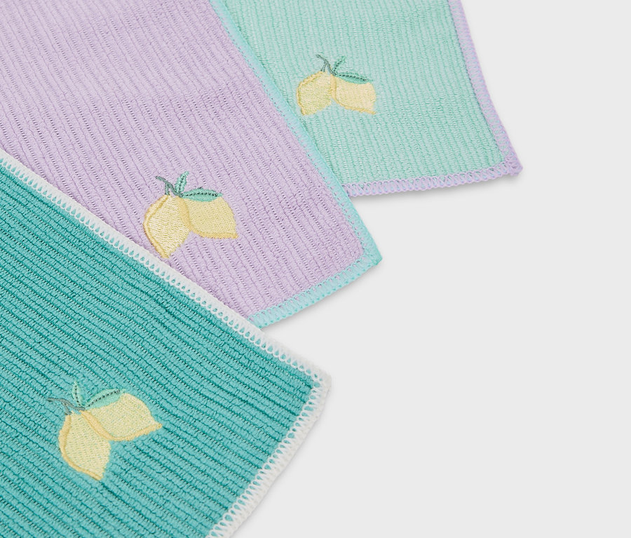 Gros plan sur trois serviettes en tissu colorées avec des broderies de citrons.