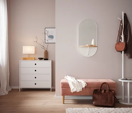Chambre avec commode blanche, miroir et banc rose.