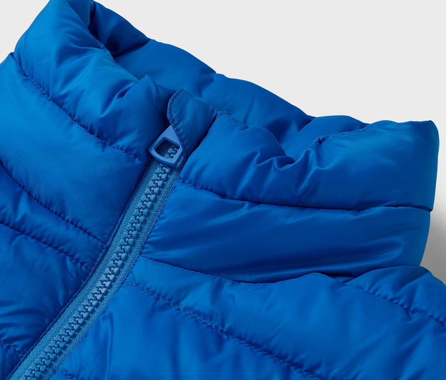 Détail d'une veste matelassée bleue avec col et fermeture éclair.