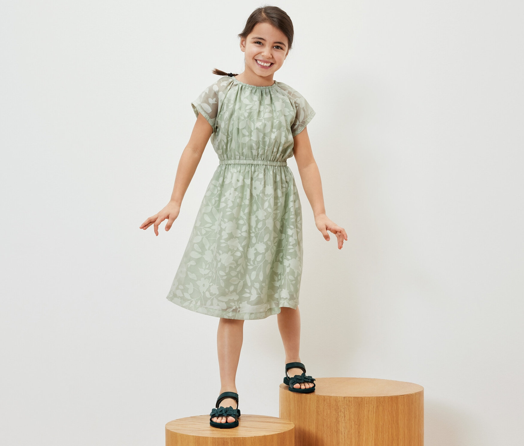 Une jeune fille souriante se tient sur des marches en bois et porte une robe pour enfant.