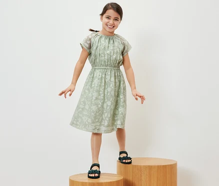 Une jeune fille souriante se tient sur des marches en bois et porte une robe pour enfant.