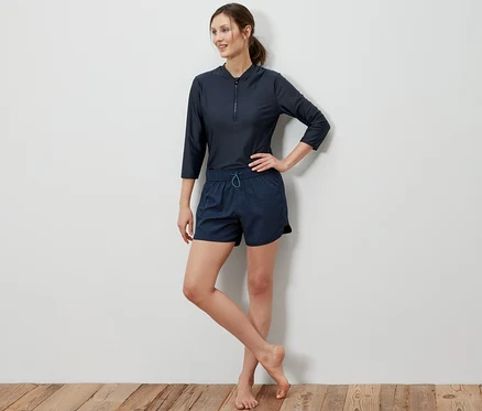 Femme posant en short de bain et haut à manches trois-quarts.