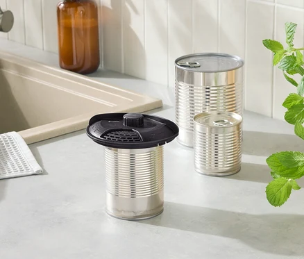 Vue rapprochée d'un comptoir de cuisine avec une boîte de conserve à couvercle noir et deux autres boîtes de conserve. Derrière elles se trouve une bouteille en verre marron.