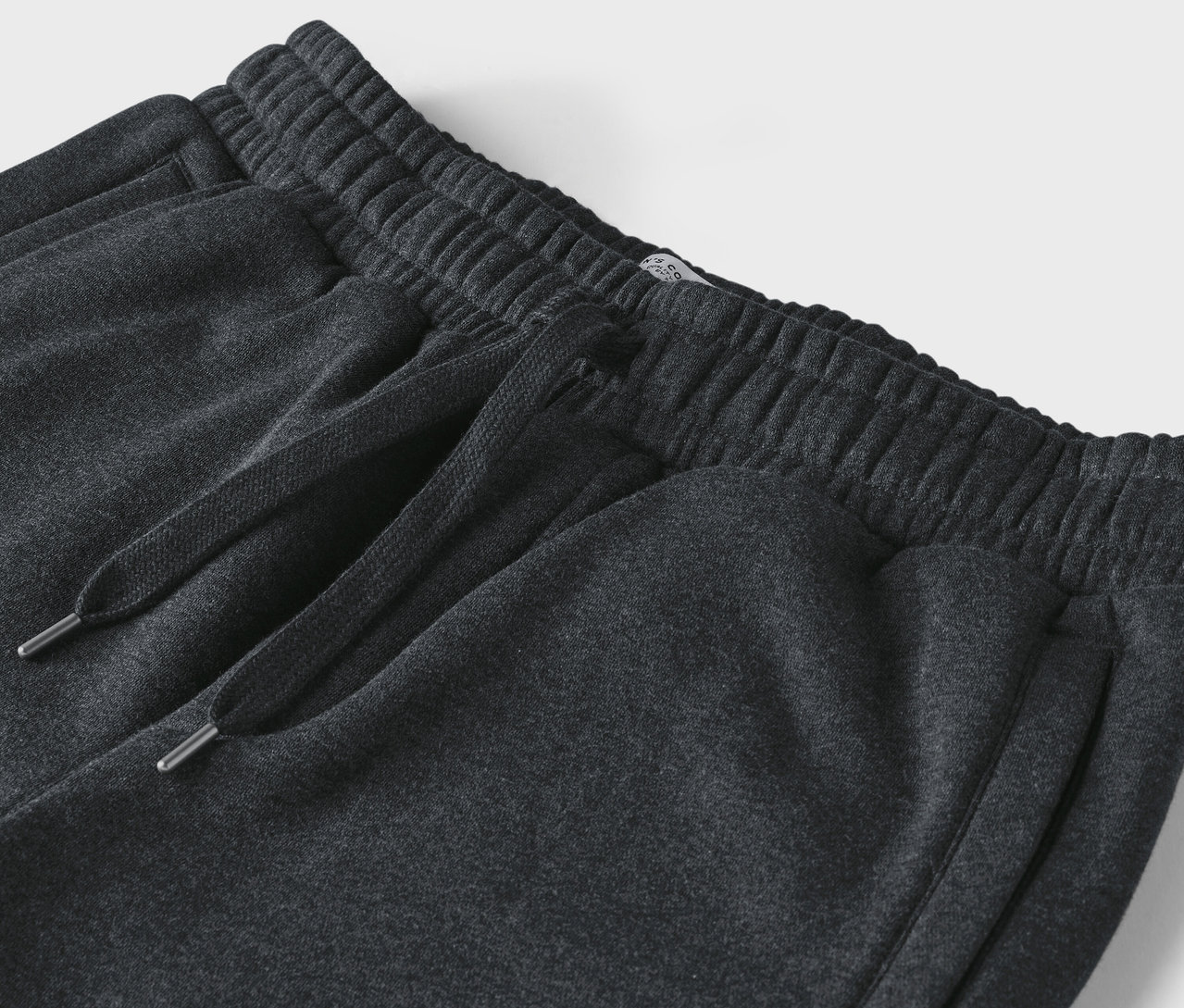 Gros plan sur un pantalon de jogging gris foncé avec cordon de serrage et taille élastique.