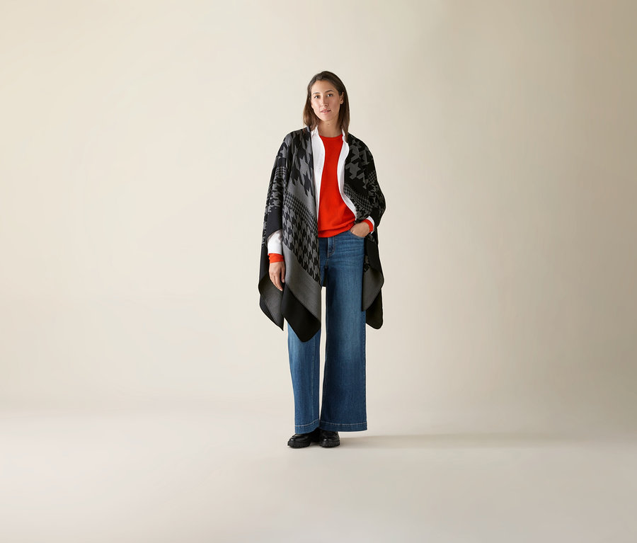 Une femme debout portant un pull orange en maille fine de laine mérinos.