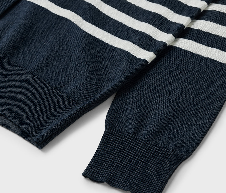 Détail d'un pull bleu marine à rayures blanches, montrant les manches et les bords côtes.