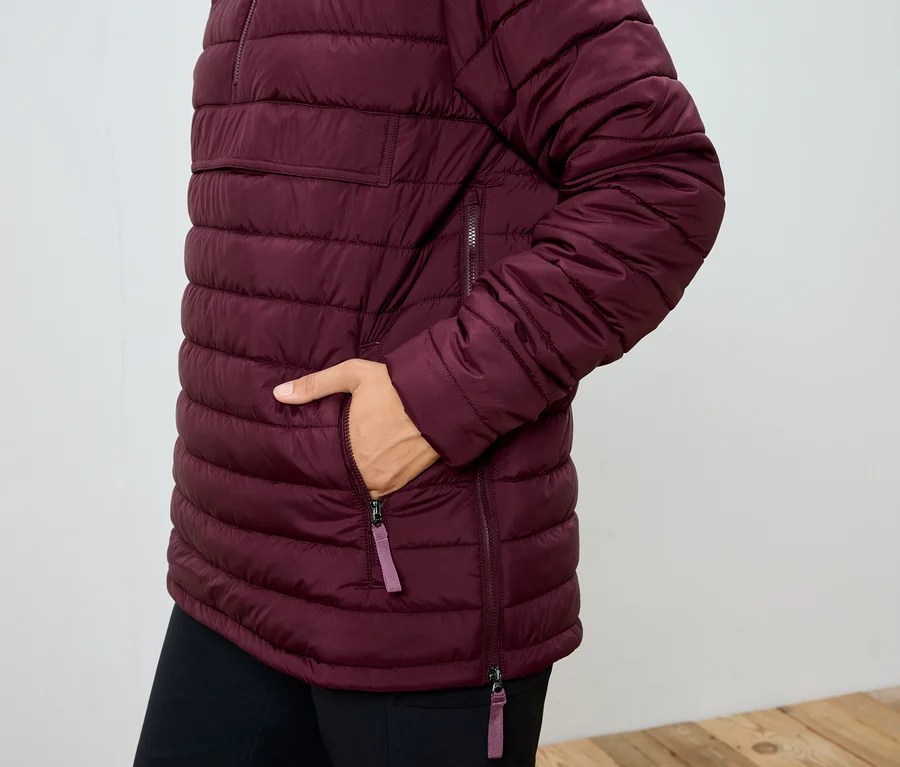 Femme avec la main dans la poche d'une veste matelassée bordeaux.