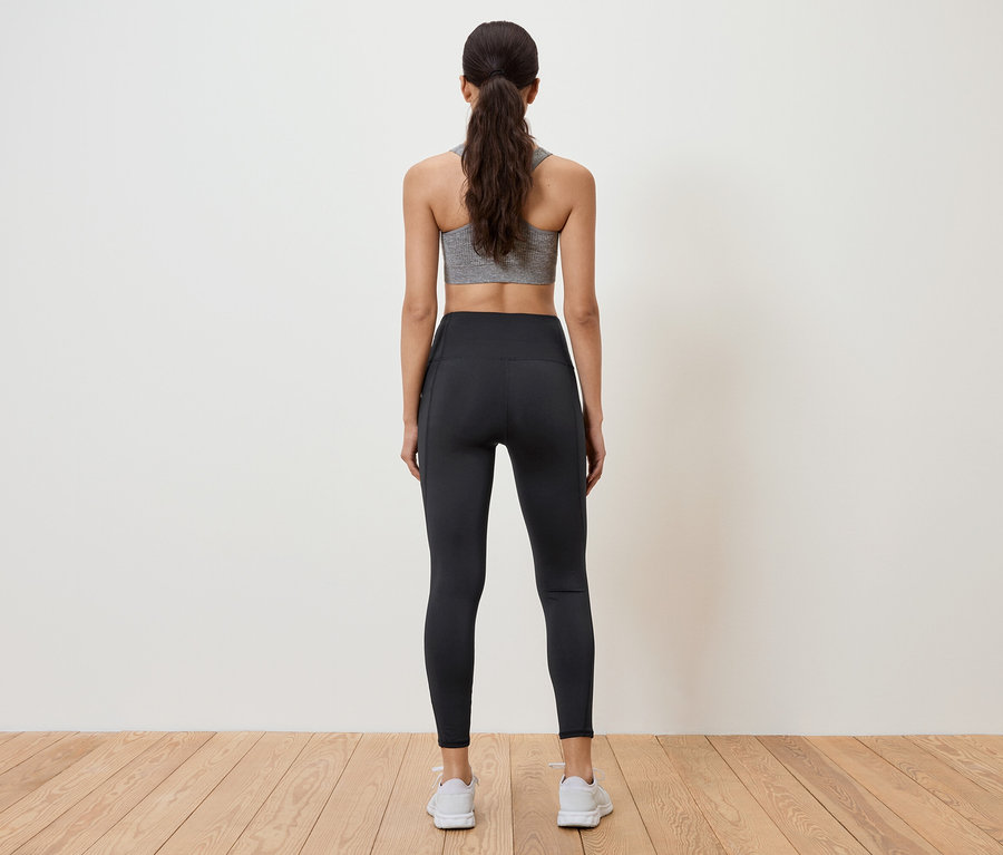 Une femme portant une brassière de sport grise et un legging noir, dos à la caméra.