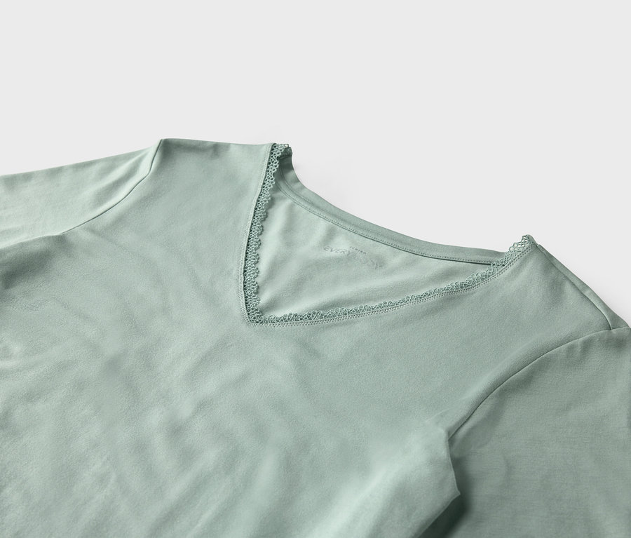 Gros plan sur un t-shirt vert clair à manches courtes avec un col en V orné de dentelle.