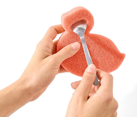 Des mains tiennent une éponge en silicone et la percent avec une cuillère.