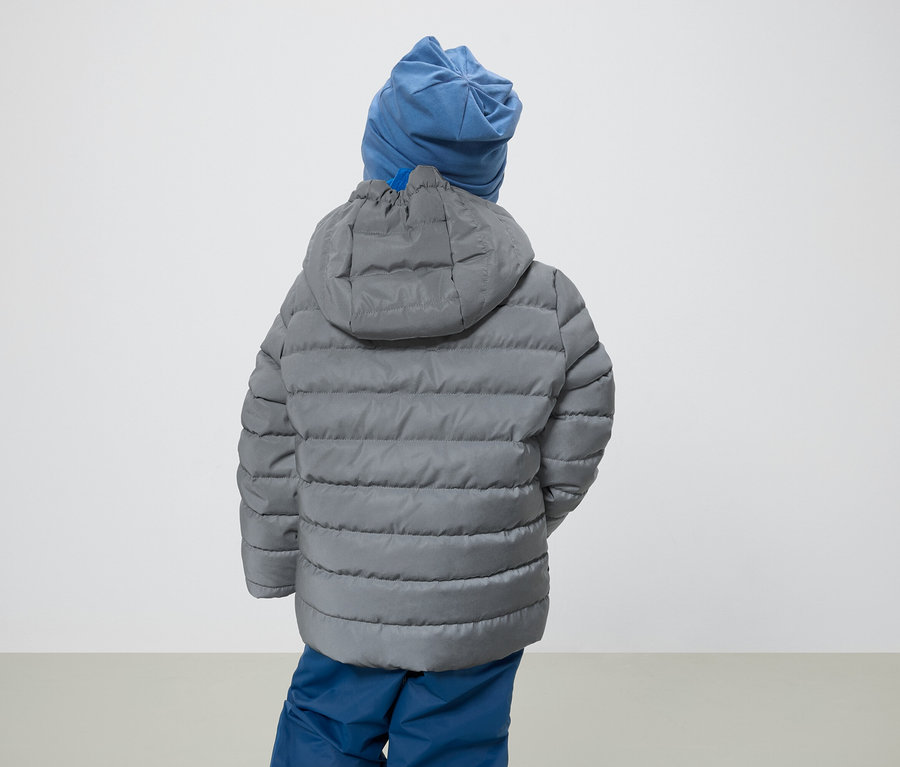 Un garçon dos à la caméra porte une veste grise à capuche et un bonnet bleu.