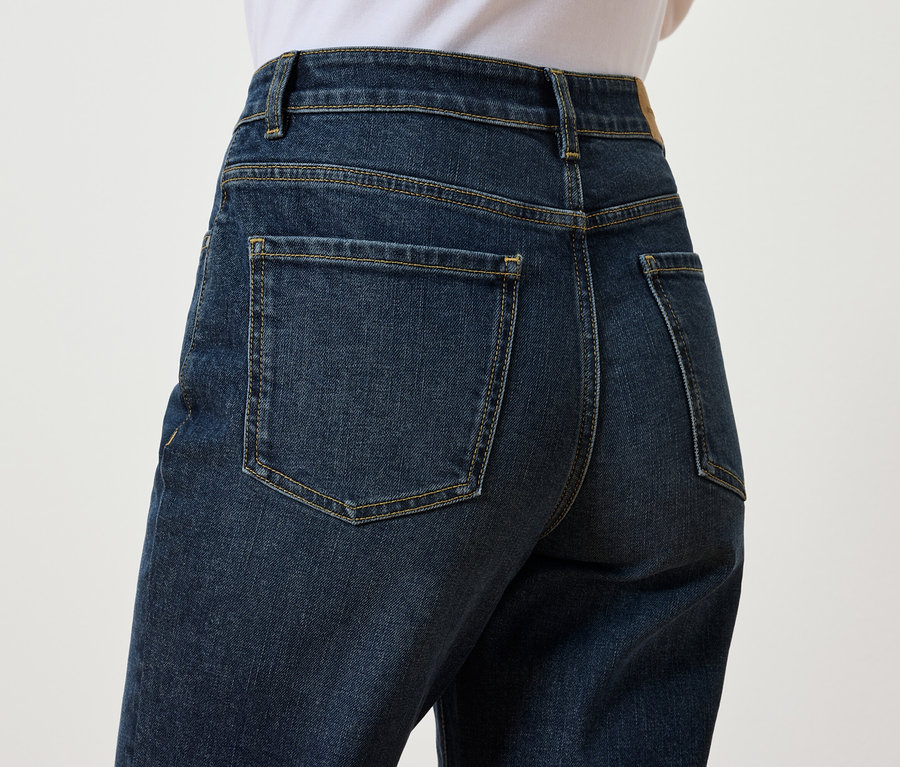 Gros plan sur l'arrière d'un jean bleu foncé porté par une personne sur un fond blanc.