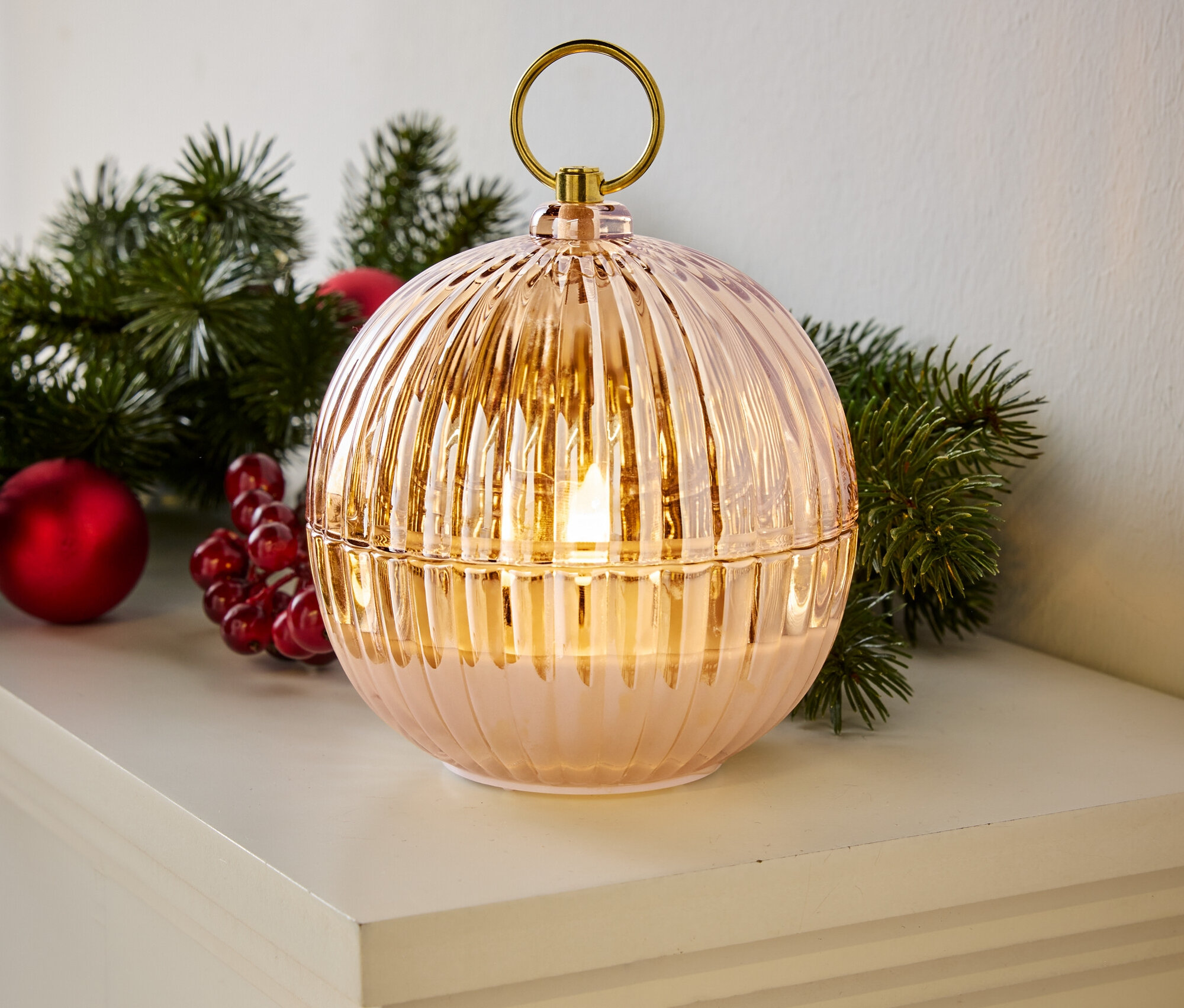 Lampe décorative en forme de boule avec une surface rainurée, une poignée dorée et une lumière LED, placée sur une étagère blanche à côté d'une décoration de Noël.