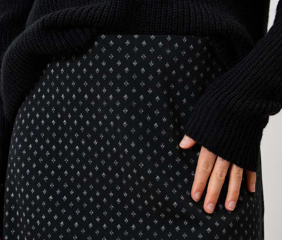 Gros plan sur une jupe noire pour femme avec un motif discret et un pull noir.