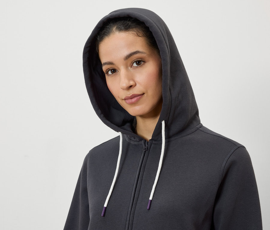 Portrait d'une femme portant un sweat à capuche gris zippé avec des cordons blancs.
