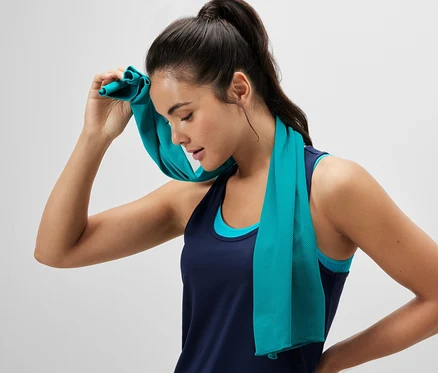 Une femme s'éponge le visage avec une serviette de sport rafraîchissante.