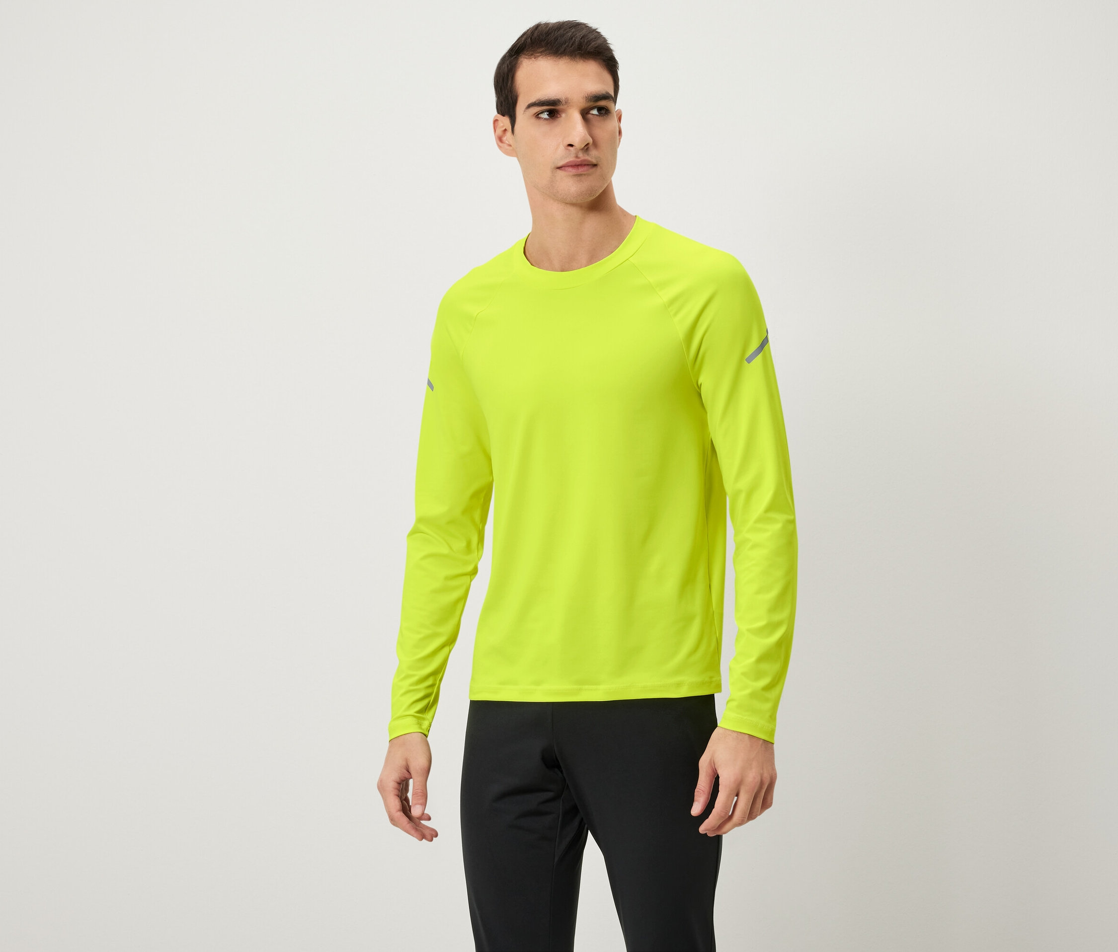 Un homme pose en t-shirt à manches longues jaune néon et pantalon de survêtement noir.