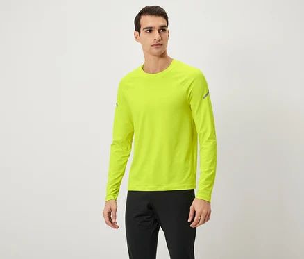 Un homme pose en t-shirt à manches longues jaune néon et pantalon de survêtement noir.