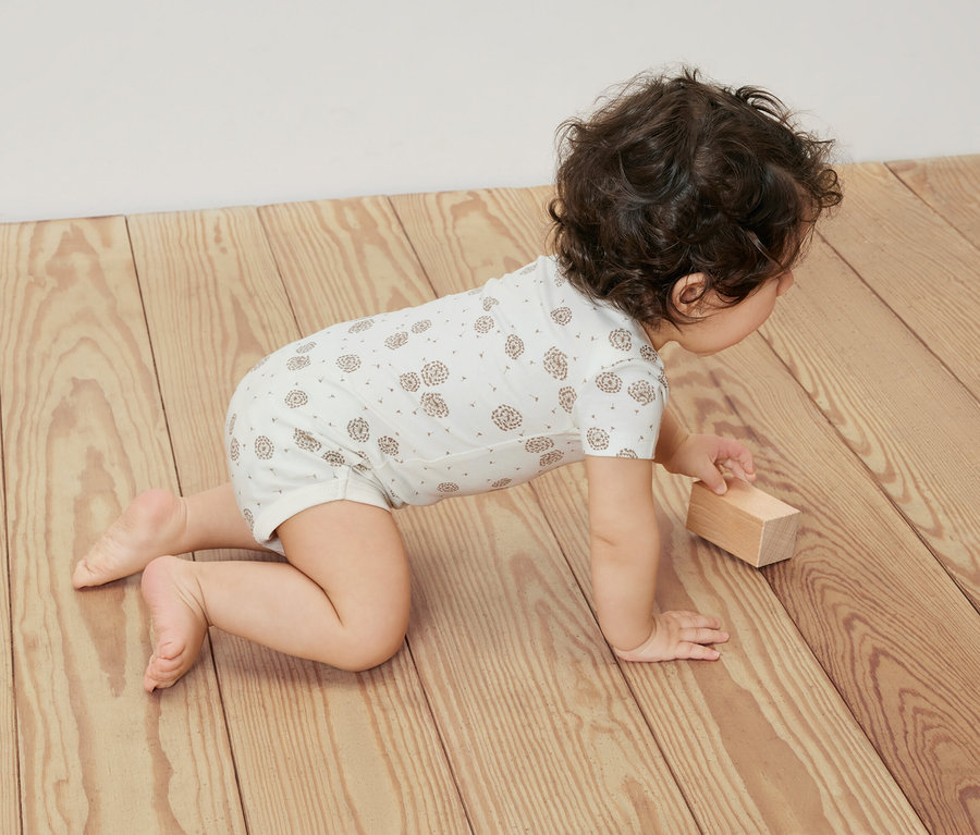 Bébé rampant sur un plancher en bois, portant un body blanc à manches courtes, lot de 5.