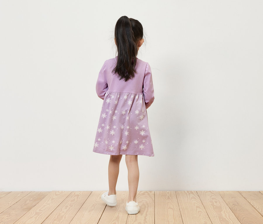 Fillette en robe lilas à étoiles et baskets blanches, dos à la caméra.