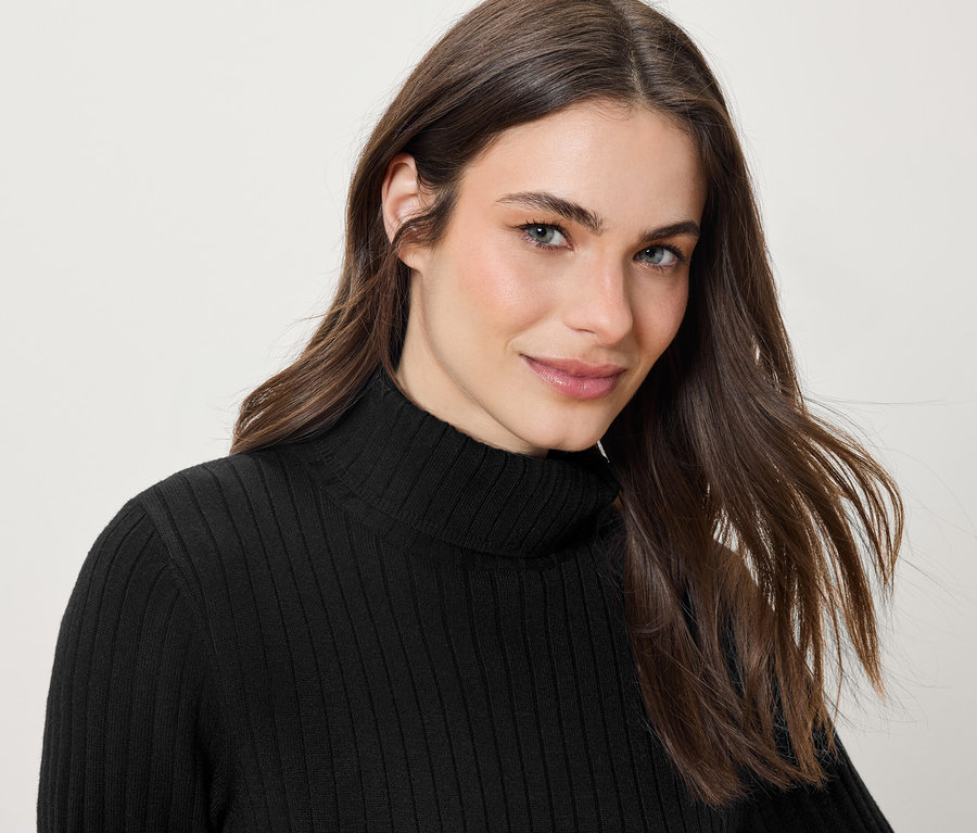 Portrait d'une femme souriante aux longs cheveux bruns portant un pull à col roulé noir.