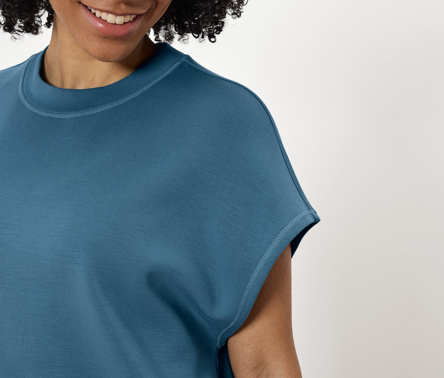Femme souriante portant un t-shirt bleu-vert.
