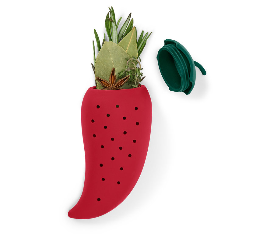 Infuseur à thé en silicone rouge en forme de poivron rempli d'herbes, avec son couvercle à côté.