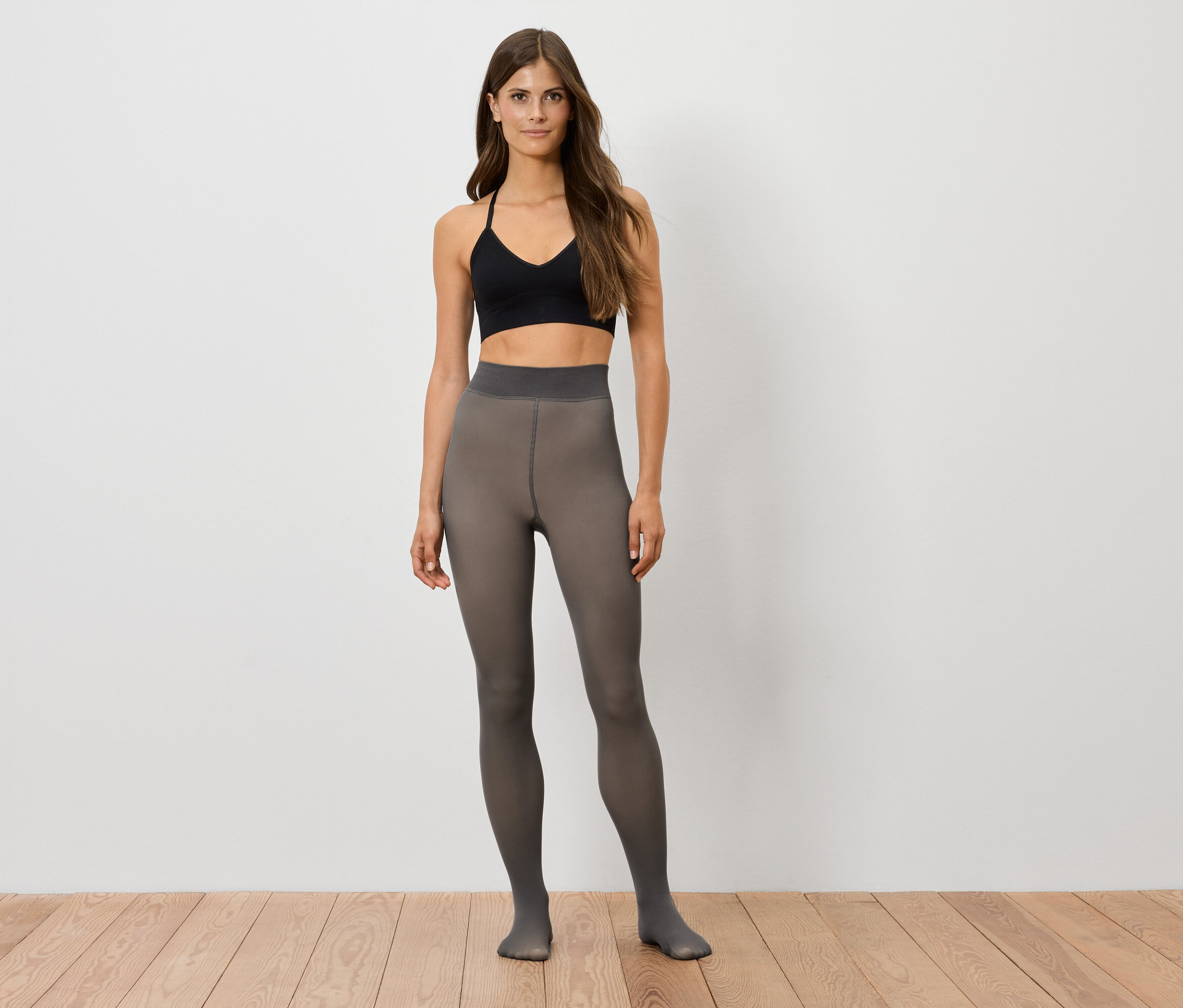 Une femme debout portant un débardeur de sport noir et des collants gris.