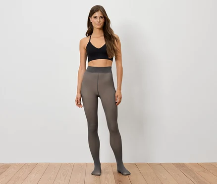 Une femme debout portant un débardeur de sport noir et des collants gris.