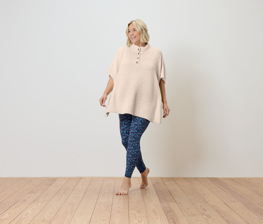 Une femme marche pieds nus sur un plancher en bois, portant une tunique crème à manches courtes et un legging bleu.