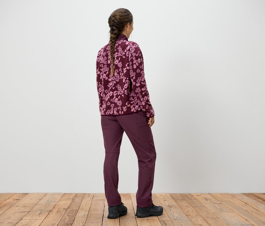 Une femme avec une tresse se tient dos à la caméra, portant un sweat-shirt violet à motifs floraux et un pantalon violet.