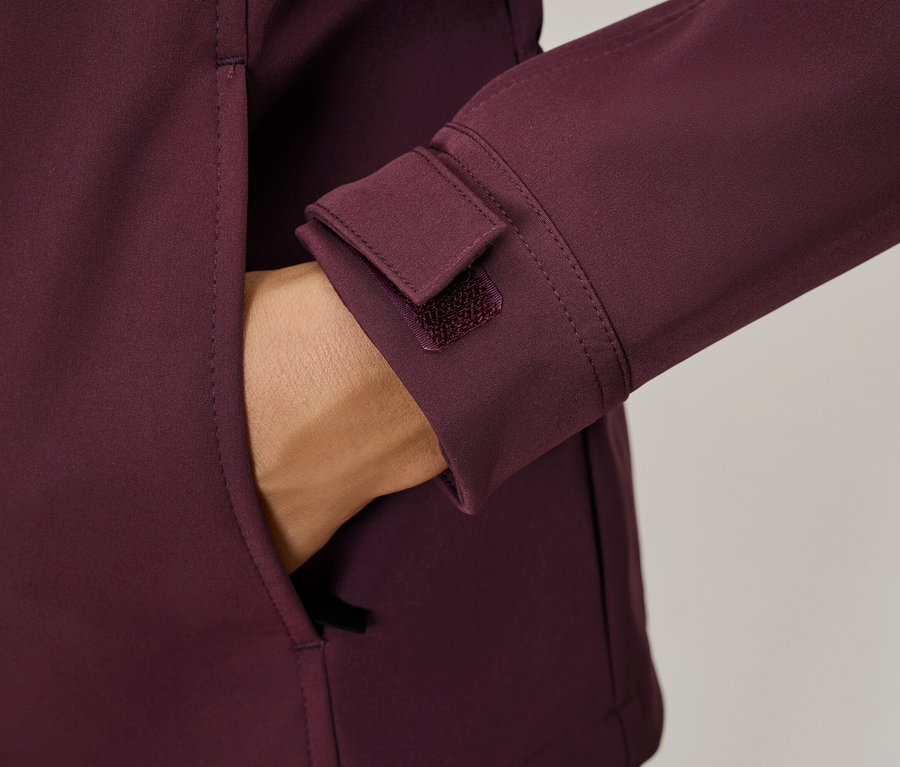 Main dans la poche d'une veste bordeaux, détails comme une manchette à scratch.