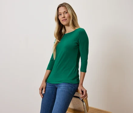 Blonde en T-shirt vert à manches trois-quarts et jean bleu assise sur une chaise.